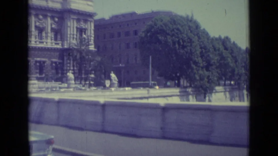 Final frame shows ornate stone architecture, a tree-lined riverside edge, pedestrians at a distance, and the top of a passing car.