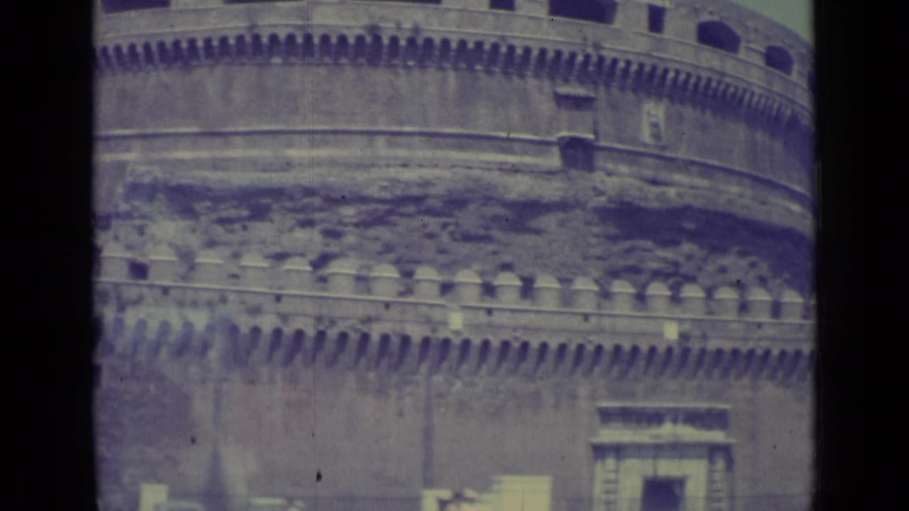 1962 8mm view of Castel Sant'Angelo's rounded stone exterior with battlements, arched openings, and partial street detail below.
