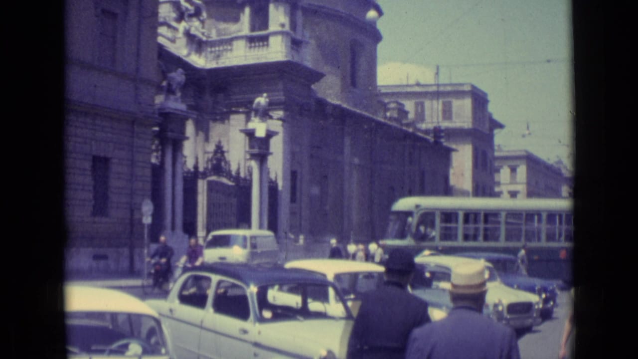 1962 Vatican City traffic view with compact cars, suited pedestrians, and a bus or trolley moving past a masonry building and balcony.