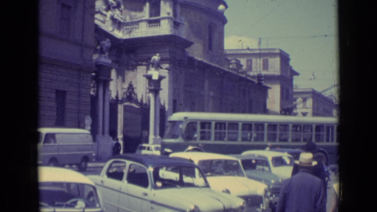 1962 Vatican City street traffic with a bus or trolley, compact cars, pedestrians, and a stone building facade with a balcony.