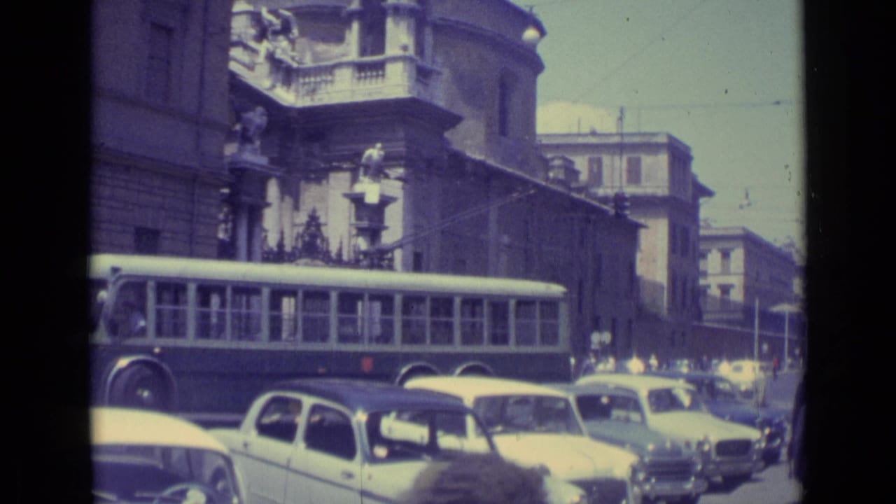 1962 Vatican City traffic scene showing a long bus among compact cars, pedestrians, street poles, and tall masonry facades.