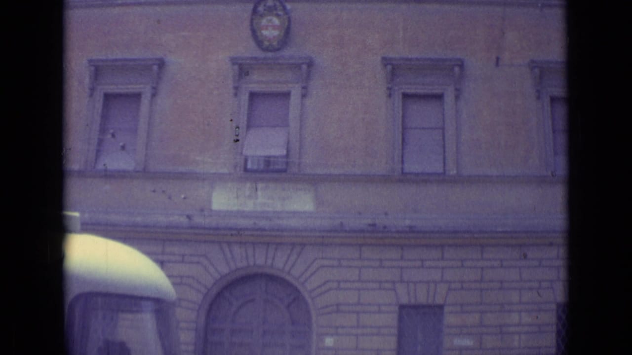 Stone building facade with shuttered windows and an emblem above the street.