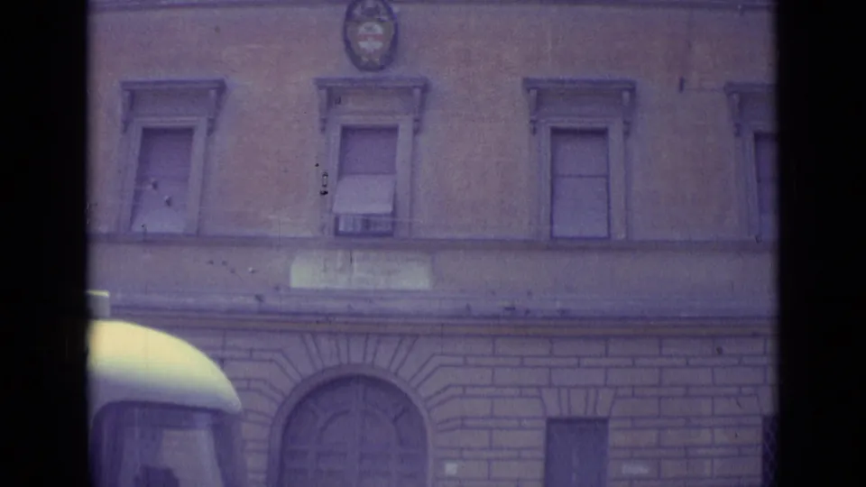 Vatican City 1962 home-movie frame showing a formal stone facade with shuttered windows and an emblem above arched ground-floor openings.