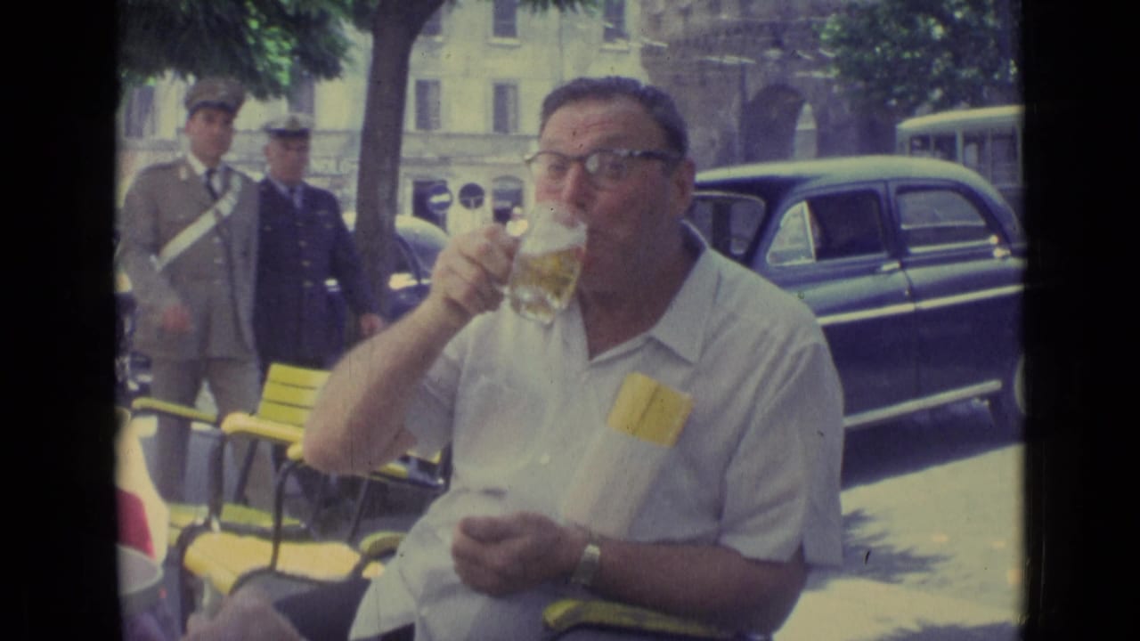 Man drinks from a glass as uniformed men and cars appear in the background.