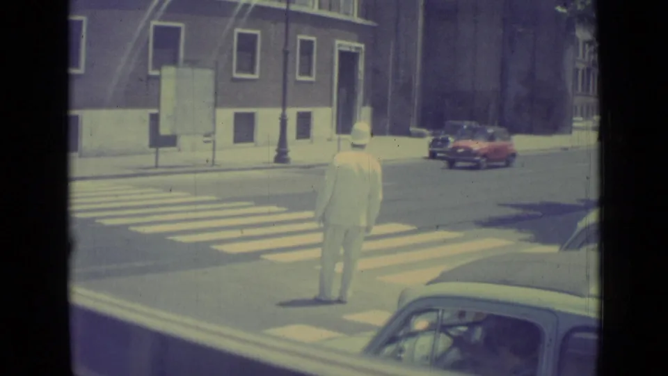 In Vatican City in 1962, a white-uniformed traffic officer stands near a crosswalk while mid-century cars move through the street.