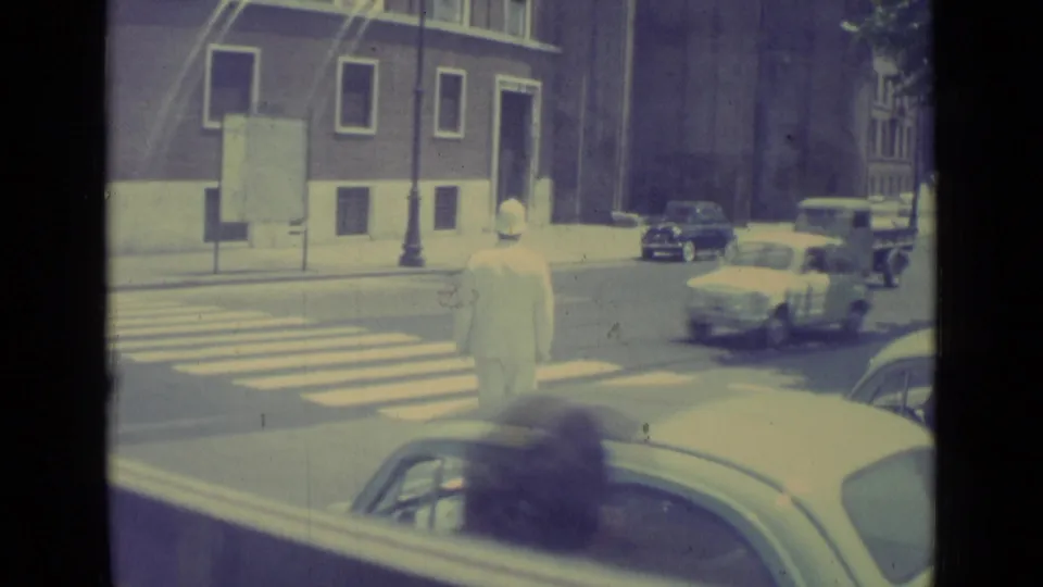 A Vatican City street scene from 1962 shows a uniformed officer at a crosswalk as cars and a small truck pass nearby.