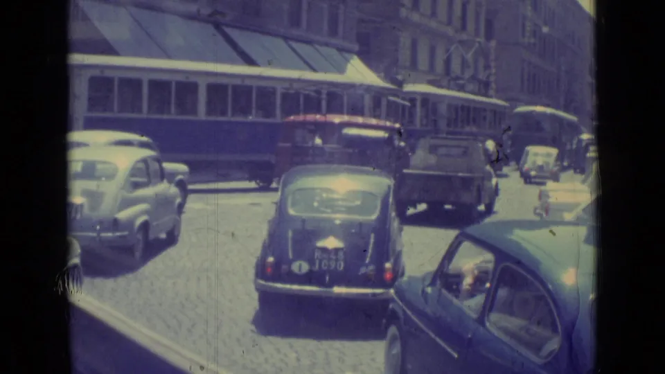 The 1962 Vatican City footage shows cars and a small truck in traffic as a tram passes behind them on a cobblestone street.