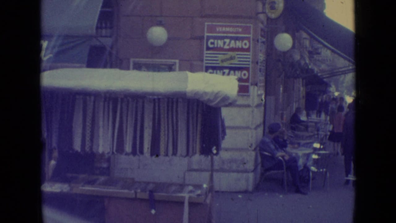 Street corner with striped awning, hanging clothes, cafe tables, pedestrians, and a Cinzano sign.