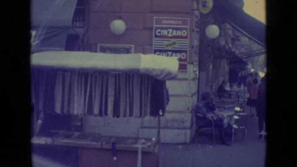 1962 Vatican City street view with a shop awning, outdoor seating, pedestrians, stone facade, globe lamps, and Cinzano advertising.