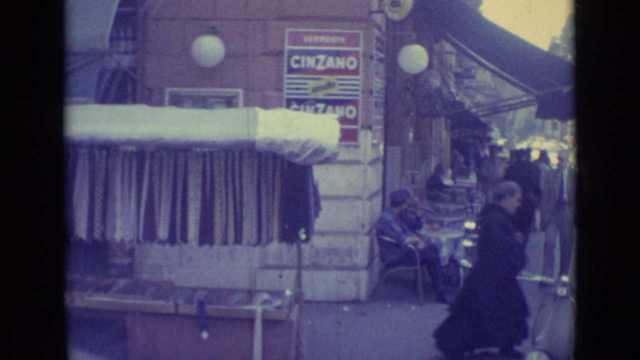 1962 Vatican City street footage showing a storefront awning, garments on display, sidewalk tables, pedestrians, and a Cinzano advertisement.