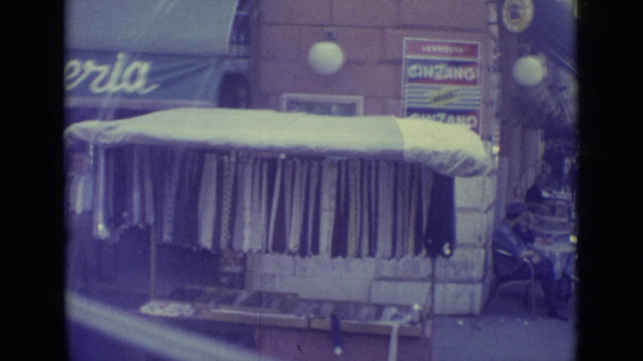 1962 Vatican City sidewalk view with a striped awning filling the frame, outdoor cafe furniture, pedestrians, and partial Cinzano signage.