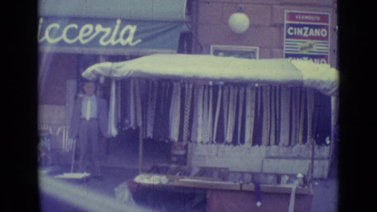 Street storefront with pasticceria awning, fabric rolls under a canopy, and a Cinzano sign.