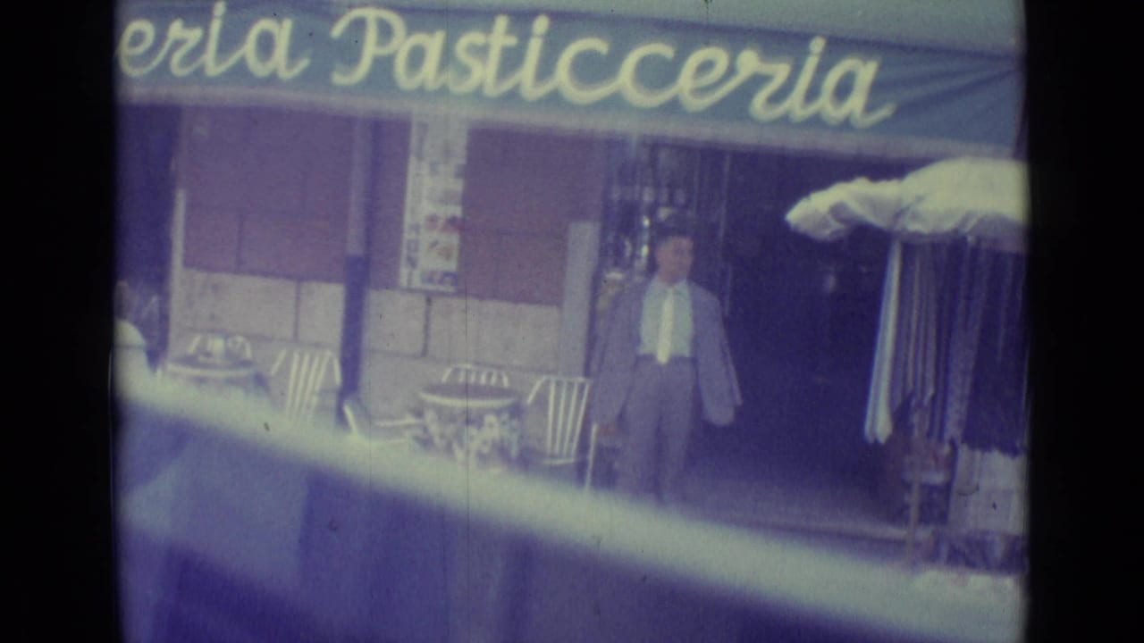 1962 Vatican City storefront scene with a suited man near a pasticceria entrance, outdoor chairs, and awning signage.