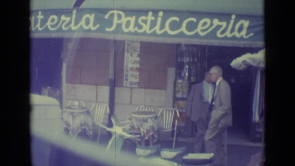 1962 Vatican City vehicle POV showing a man walking past cafe seating beneath a gelateria and pasticceria awning.