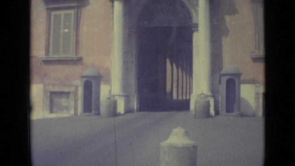 1962 Vatican City home-movie frame showing a stone facade with an arched entrance, pale columns, shuttered windows, and soft faded color.