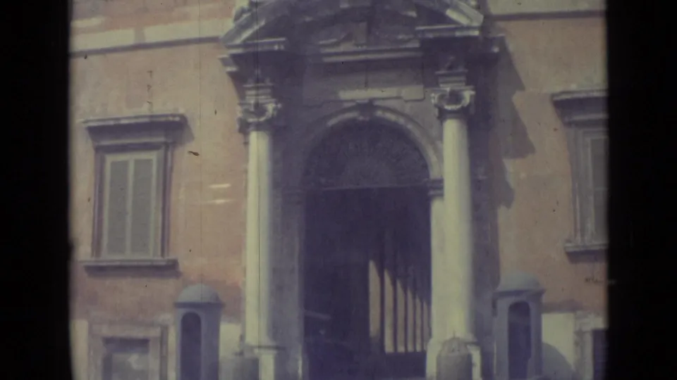 Visitor-shot 1962 Vatican City view of a grand entrance with columns, decorative arch details, windows, and muted 8mm color.