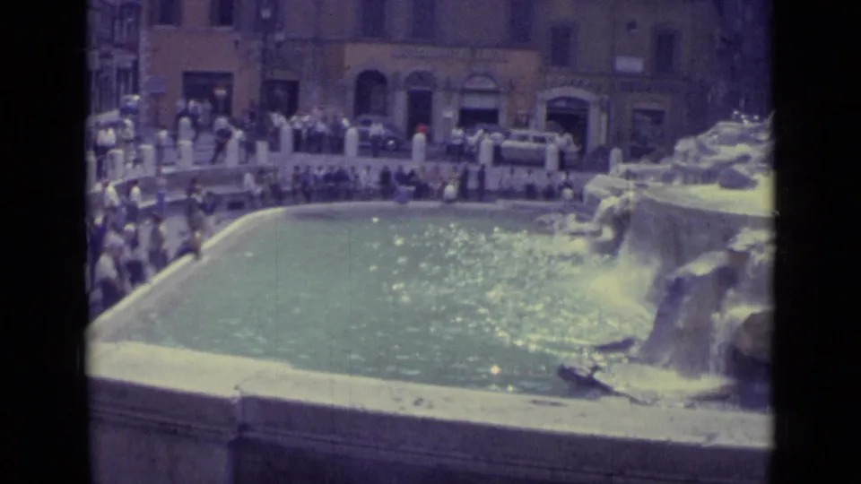 1962 8mm travel frame showing Trevi Fountain water, stone sculpture, and tourists standing around the basin.