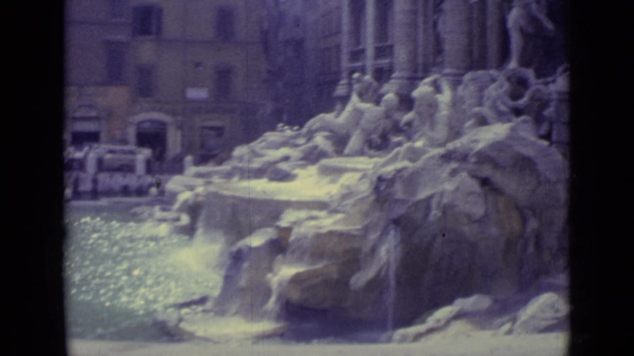 1962 8mm frame of Trevi Fountain sculptural rockwork and flowing water with visitors visible behind the basin.