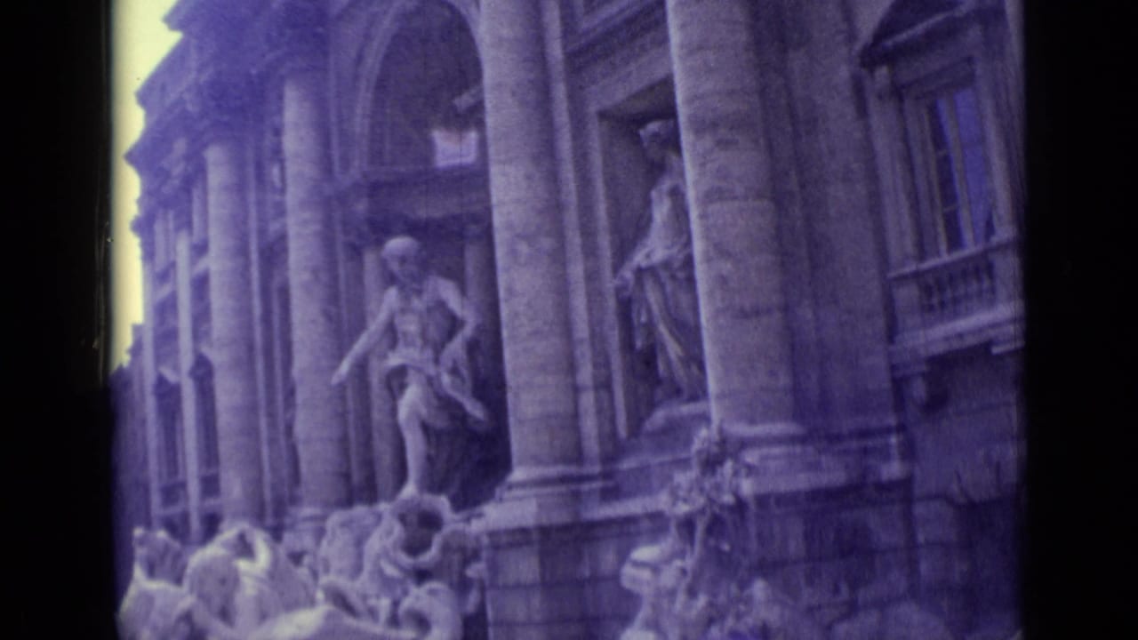 1962 8mm frame showing Trevi Fountain statues, columned facade, and sculptural details in soft faded color.