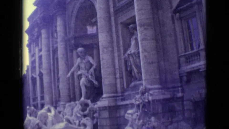 1962 8mm frame showing Trevi Fountain statues, columned facade, and sculptural details in soft faded color.