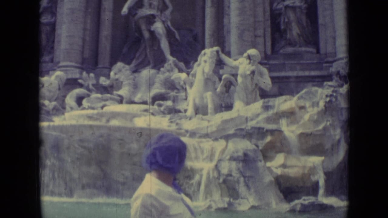 The woman faces the fountain, her purple headscarf visible against the stone sculptures and cascading water.