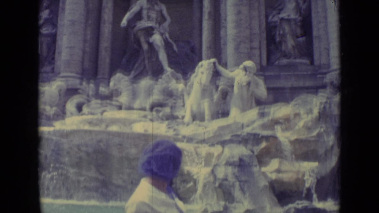 A rear view of the woman in a purple headscarf near the fountain, with sculpted figures and water filling the frame.
