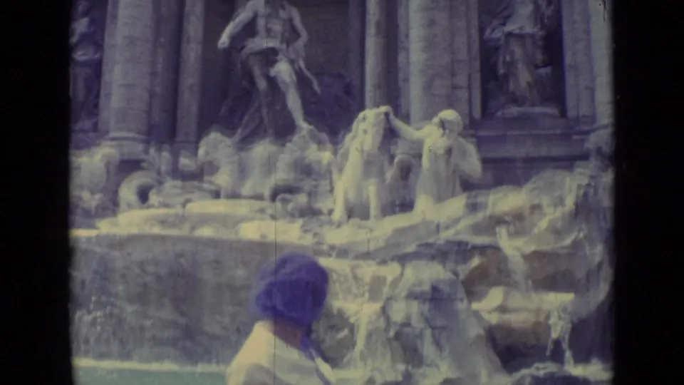 A rear view of the woman in a purple headscarf near the fountain, with sculpted figures and water filling the frame.