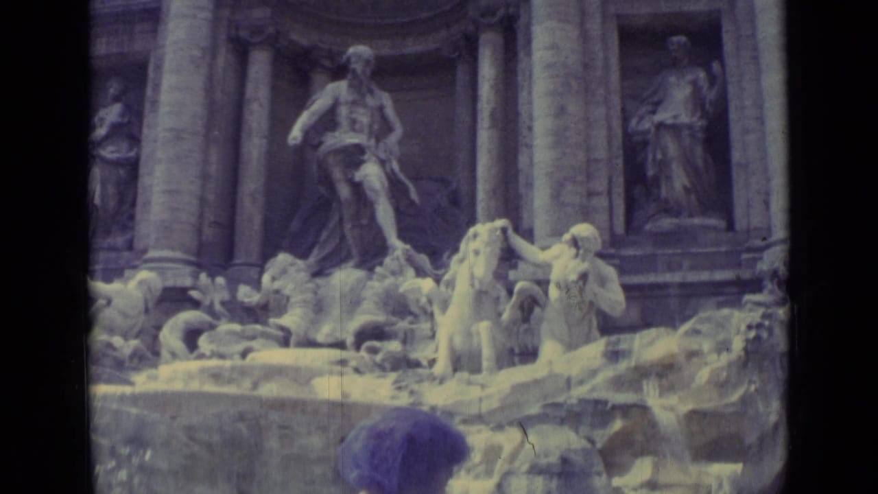 The frame centers on the fountain's sculpted figures and cascading water, with the woman's purple headscarf partly visible below.