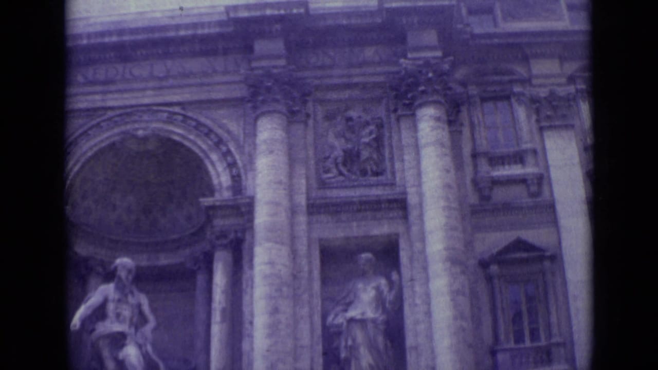 Stone facade with tall columns, arched opening, statue niche, and carved panels.