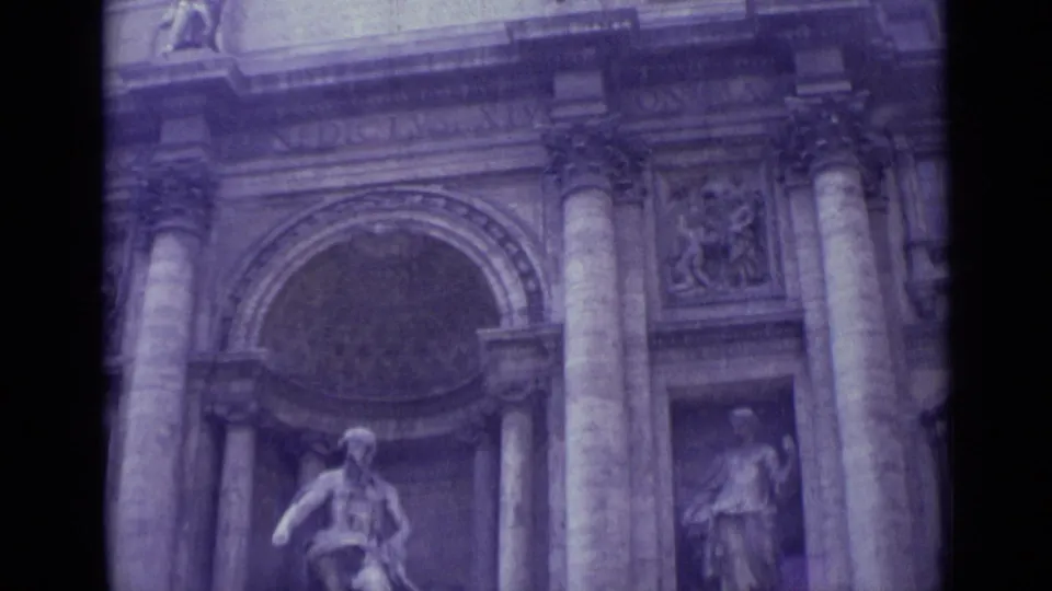 1962 8mm frame of the Trevi Fountain facade, showing tall columns, an arched niche, and a central stone sculpture.