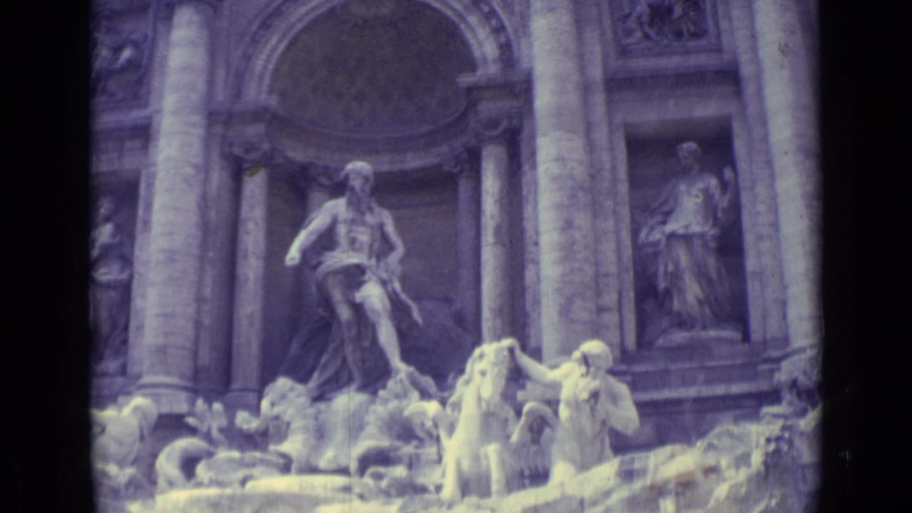 1962 home-movie frame showing the Trevi Fountain's sculptural group, tall facade columns, basin figures, and bright water highlights.