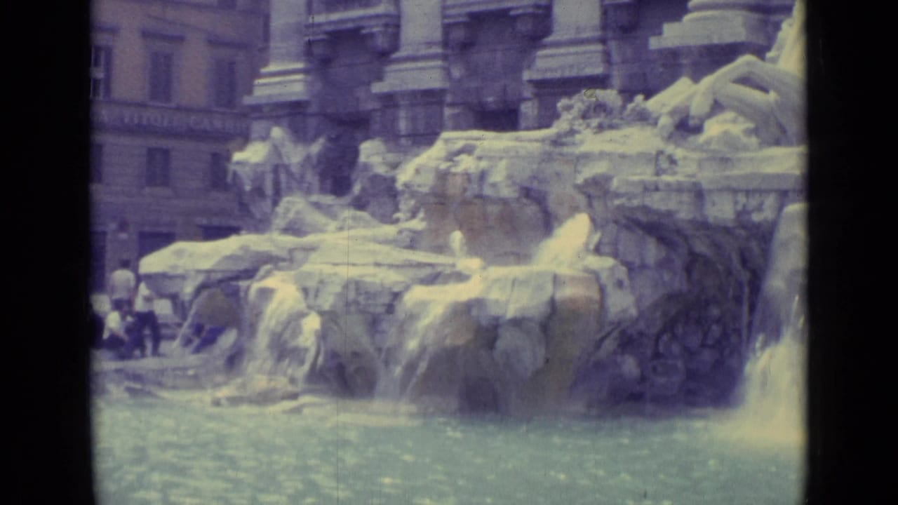Lower Trevi Fountain view in 1962 8mm footage, showing carved rocks, flowing water, statues, and small visitors near the edge.