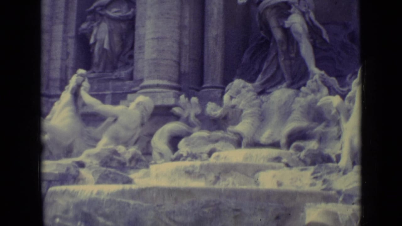 1962 home-movie frame centered on fountain statuary, including a large draped figure, horse form, columns, and flowing water.