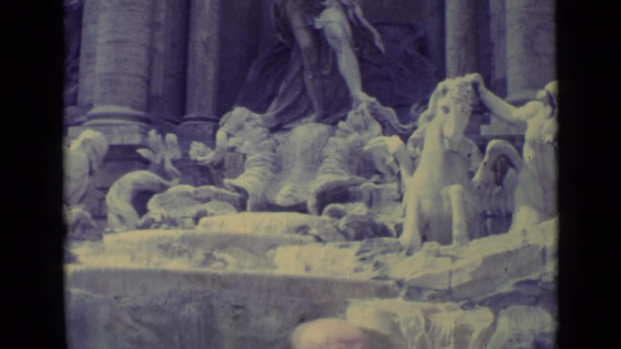 Aged 8mm frame of the fountain's sculptural group with a standing horse, carved figures, columns, and pale cascading water.