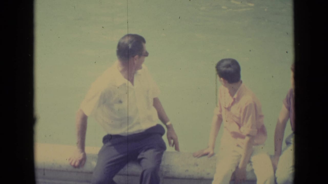 1962 Vatican City home-movie frame of two male visitors seated by water, appearing to talk beside the fountain ledge.