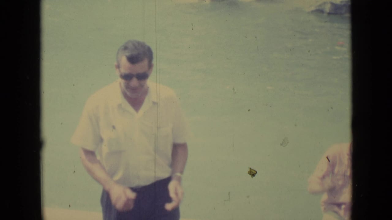 In Vatican City travel footage from 1962, a man in sunglasses smiles toward the camera near a pale water or sky backdrop.