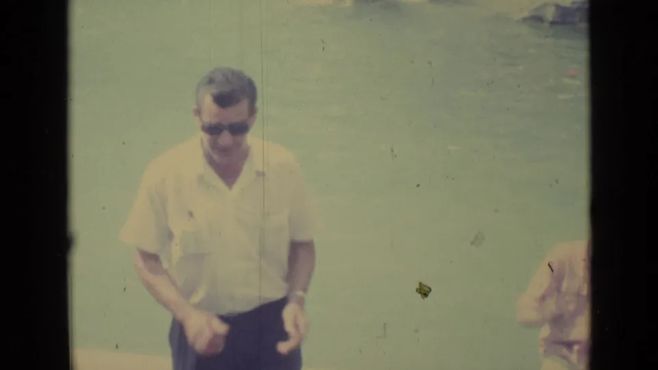 In Vatican City travel footage from 1962, a man in sunglasses smiles toward the camera near a pale water or sky backdrop.