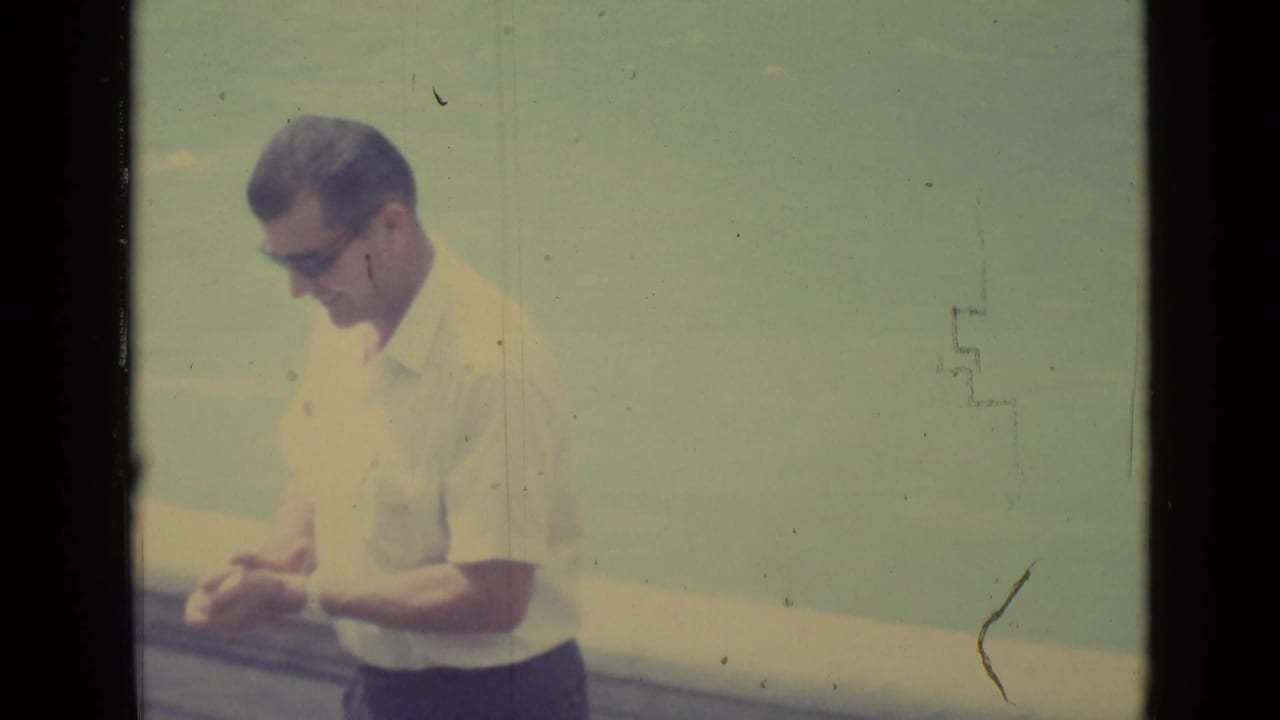The same adult man in 1962 Vatican City footage looks down at his hands, with a pale open background behind him.