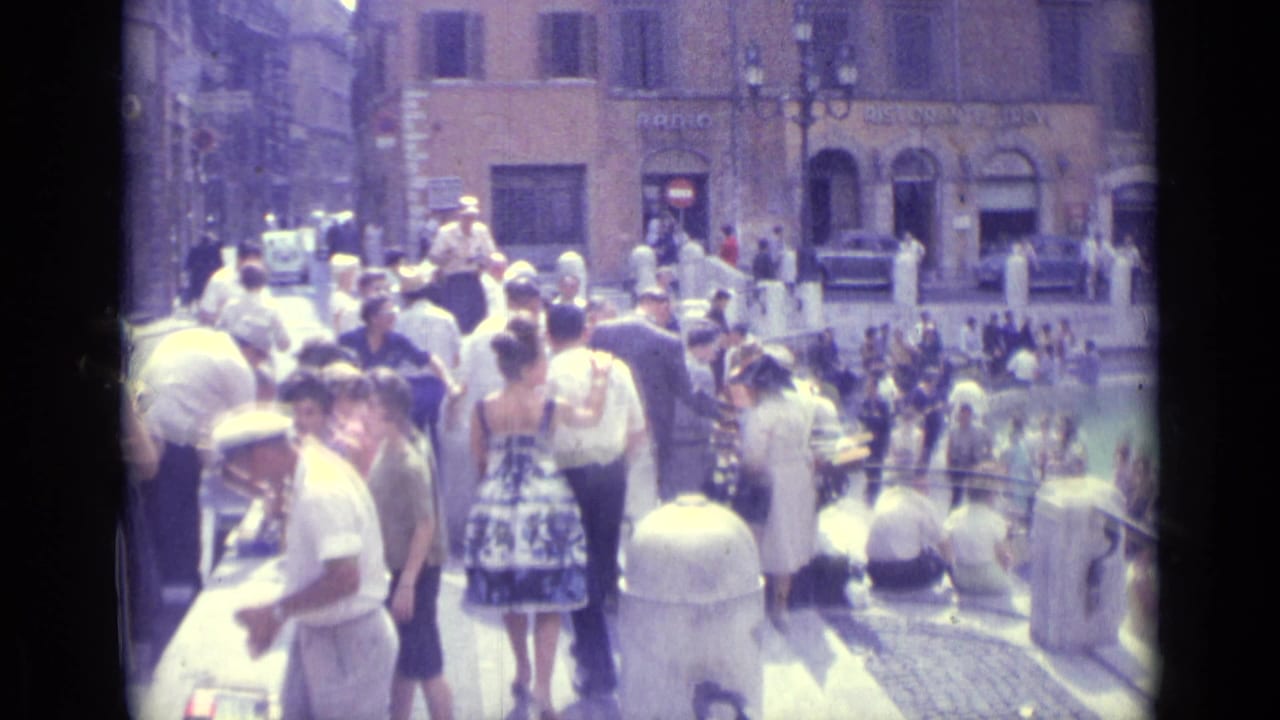 1962 Vatican City street scene with tourists or pedestrians in summer clothing walking among bollards near surrounding buildings.
