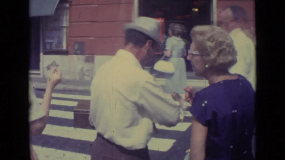The vendor appears to show or sell small items to a woman in a purple dress on a Vatican City street in 1962.