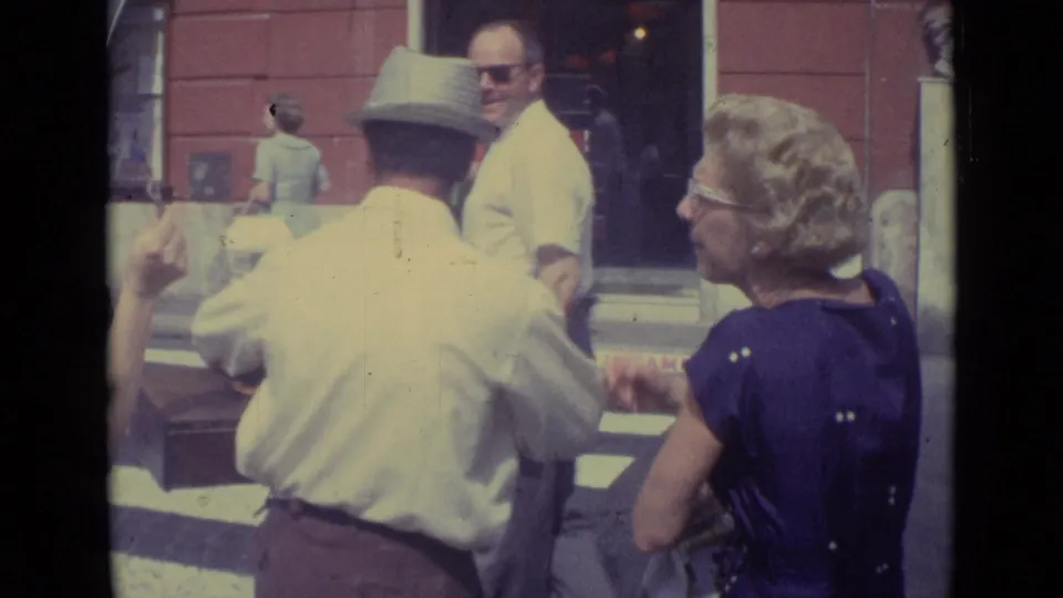 From behind the vendor, pedestrians cluster near a crosswalk while a woman in a purple dress watches the street exchange.
