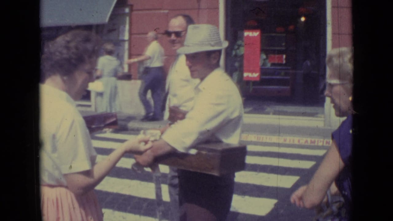 A woman reaches toward the vendor's hand or goods as he carries a wooden box on a Vatican City street in 1962.
