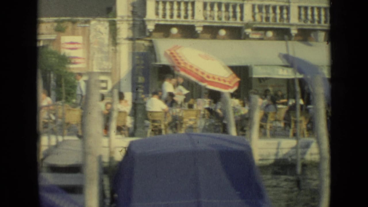 Venice, Italy, 1962, with cafe patrons under umbrellas and gondola covers crossing the canal foreground.