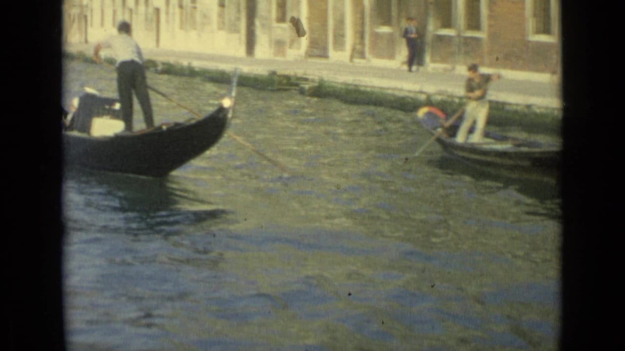 Venice canal scene from 1962 showing a gondolier standing in a black gondola and another person rowing a small boat nearby.