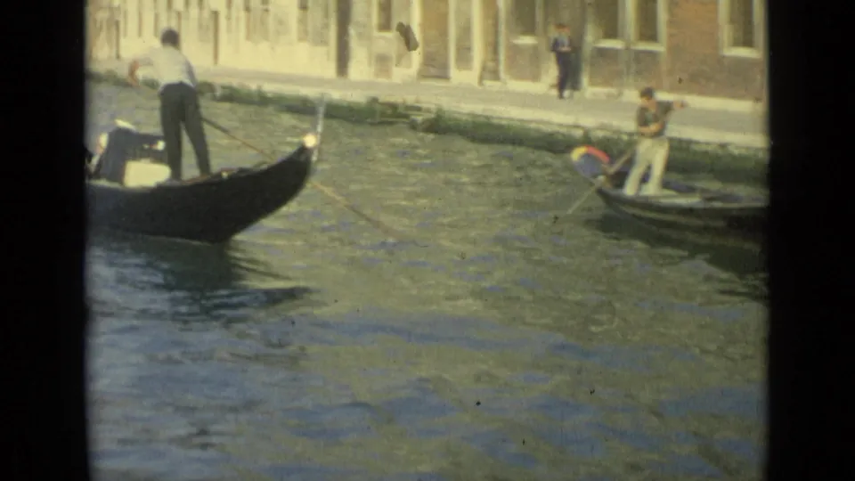 Venice canal scene from 1962 showing a gondolier standing in a black gondola and another person rowing a small boat nearby.