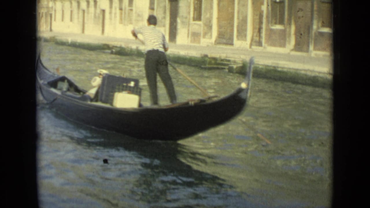 Black gondola passes through canal water with gondolier standing at the stern.