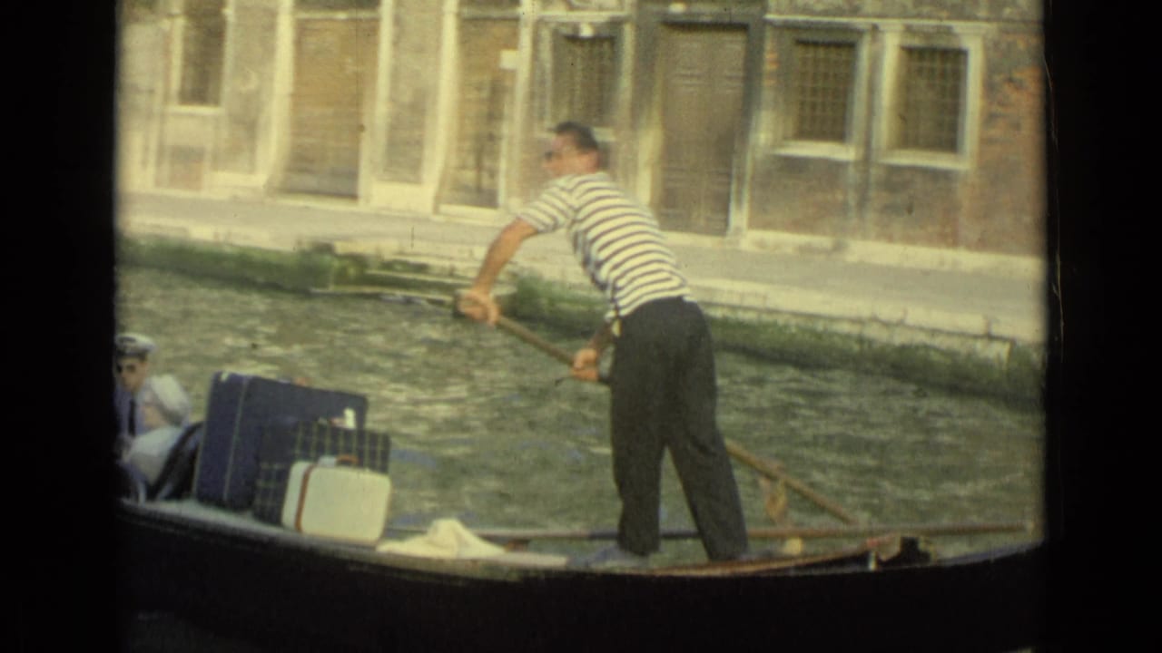 1962 Venice home-movie still of a gondolier rowing a gondola with passengers and luggage along a canal.