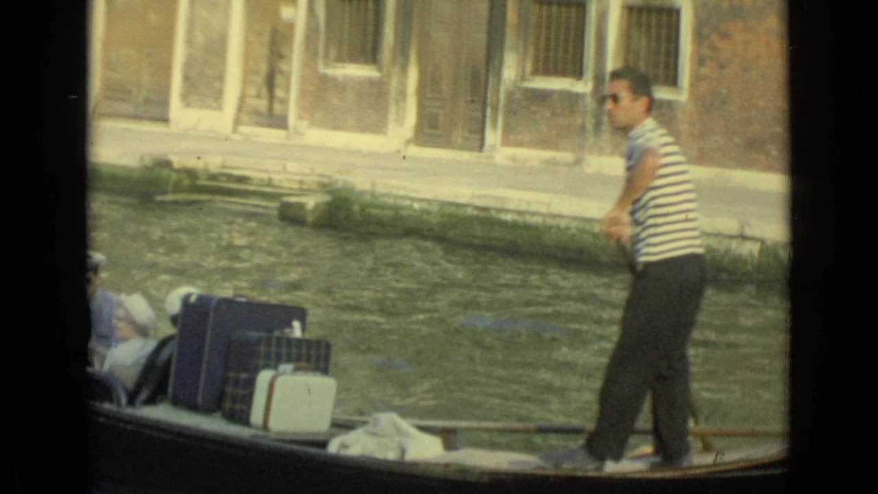 Gondolier in a striped shirt rows beside luggage on a canal boat.