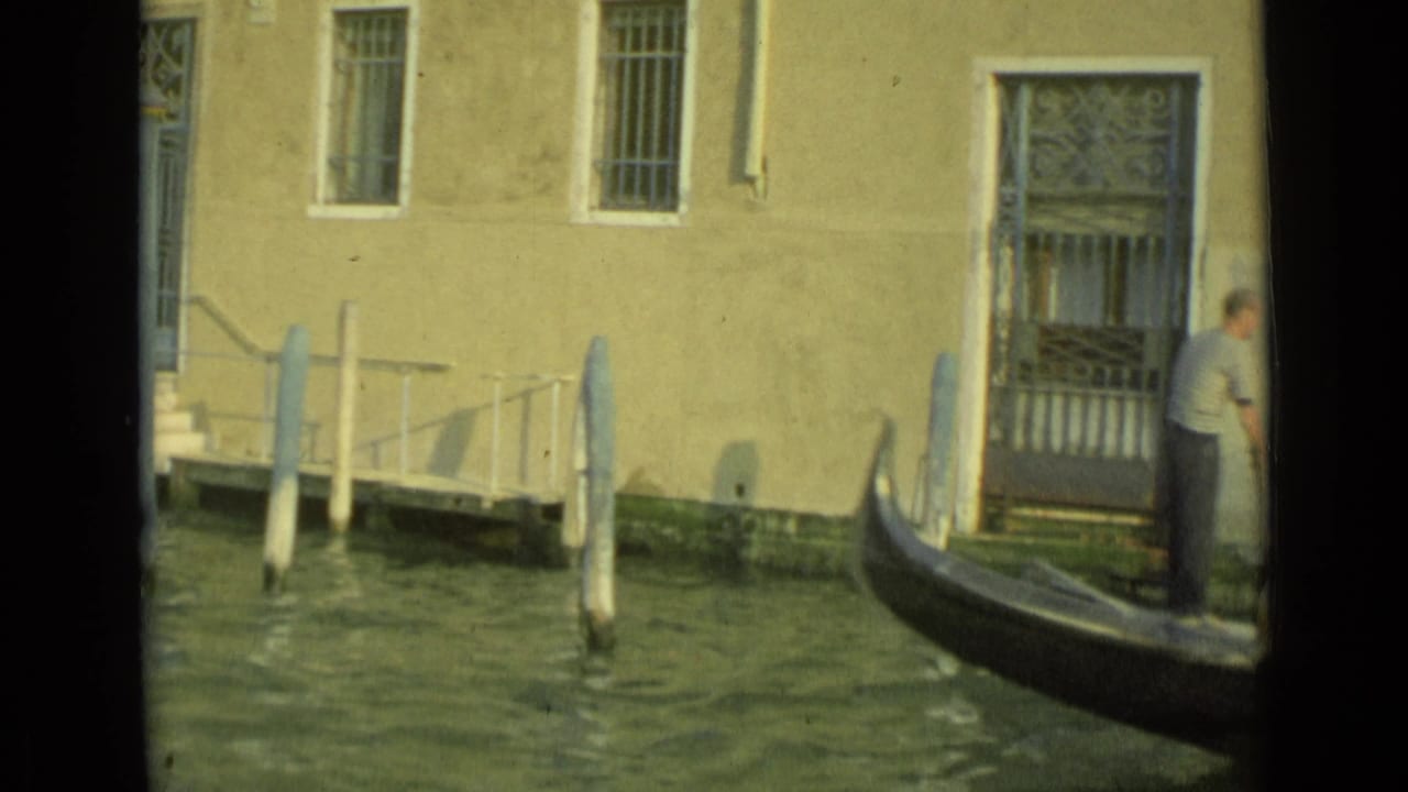 Gondola moving past a stucco canal-side building with barred windows and a doorway.