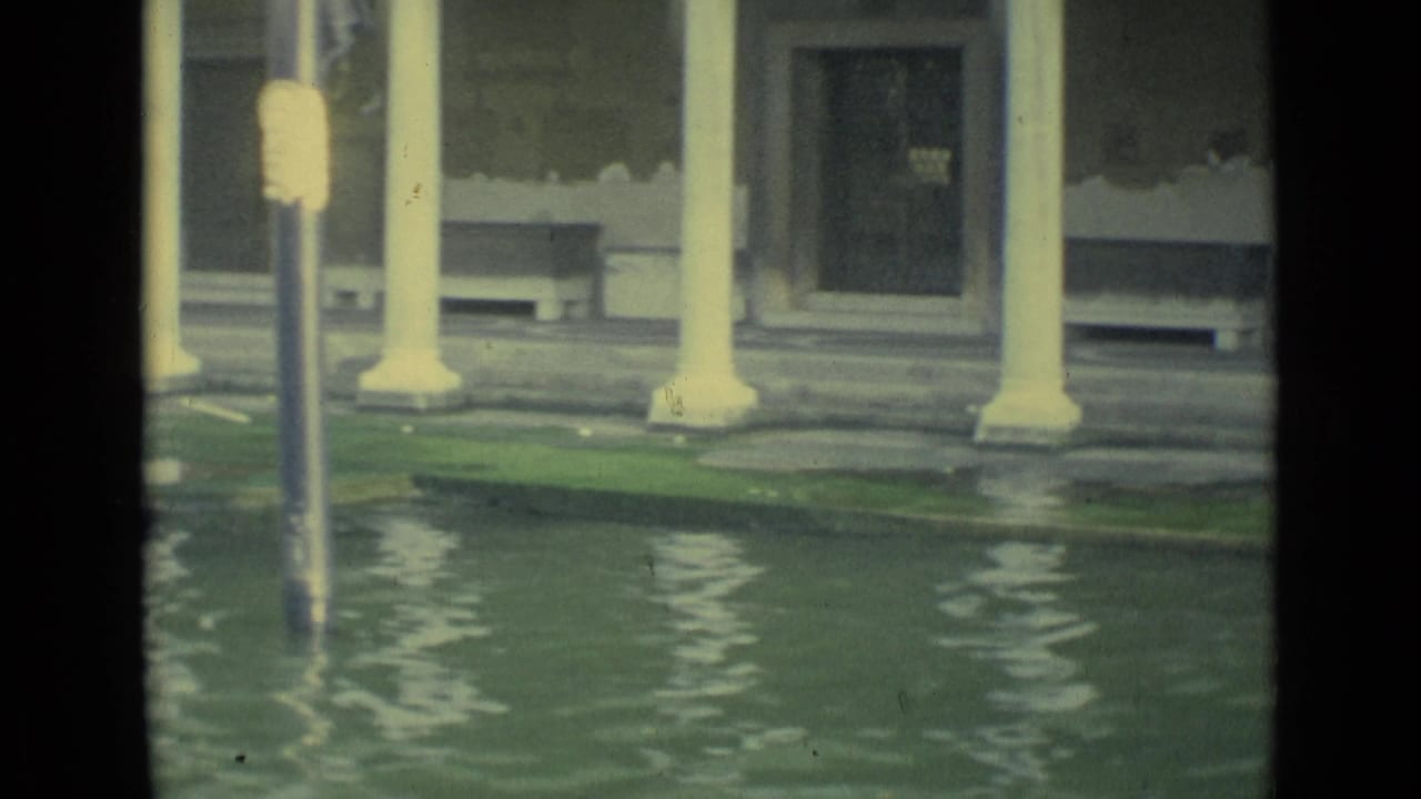 Flooded Venice canal edge with pale columns, reflections, and a partially submerged lamppost.